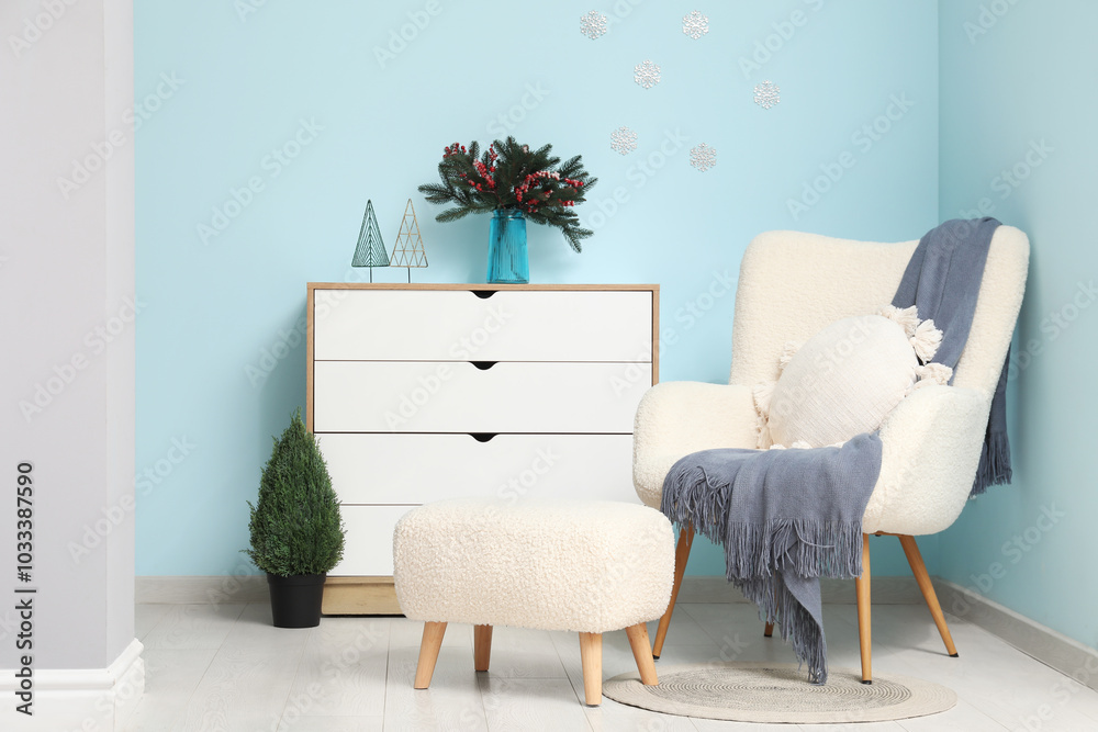 Wall mural Interior of living room with pouf, armchair, chest of drawers and Christmas decor near blue wall