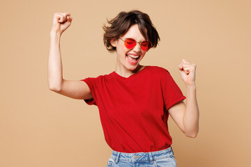 Young excited happy woman wear red t-shirt casual clothes sunglasses doing winner gesture celebrate...