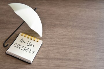 A notepad with the question "Are You Covered?" and an umbrella. Copy space for text. Insurance coverage concept.