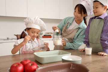 Female Asian chef with her little children making dough in kitchen