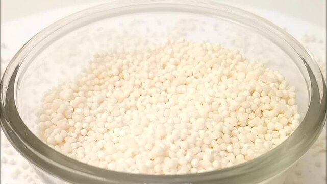 Sago pearls or tapioca pearls drops in a rotating glass bowl on white background with spices spilled around it, micro shot, center frame, herbs and spices