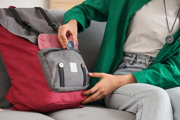 Female tourist putting compass into backpack on sofa at home, closeup