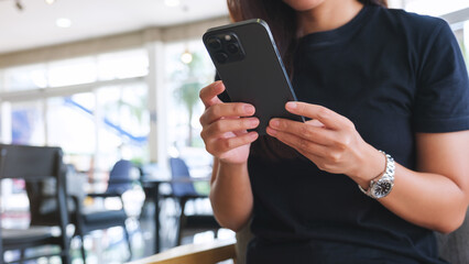 Closeup image of a woman holding and using mobile phone in cafe