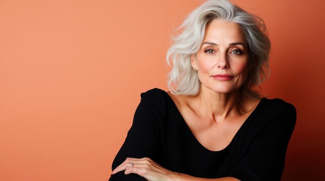 A mature woman with grey hair poses elegantly against an orange backdrop, highlighting grace, wisdom, and confidence with a modern and sophisticated feel.
