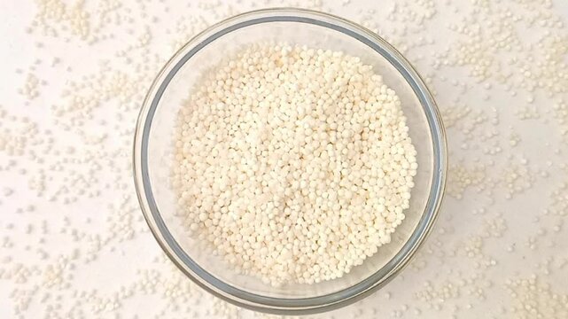 Sago pearls or tapioca pearls in a glass bowl spices spilled around it, rotating on white background, center frame, top view, close up, herbs and spices