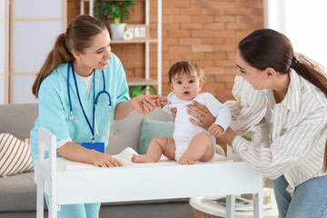 Female pediatrician with little baby on changing table and mother at home