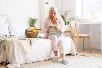 Mature woman knitting with needles in bedroom