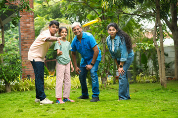 Fototapeta premium Indian Asian family enjoying outdoor playtime as teenage son teaches small sister to throw frisbee
