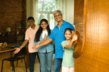 Indian Asian family happily welcoming guests at home by opening large wooden entrance door