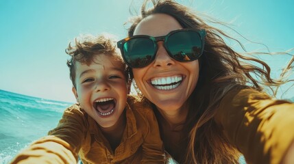A mother and her son take a delightful selfie at the beach, both laughing heartily, with their sunglasses shielding them from the bright sun and sparkling ocean waves behind.