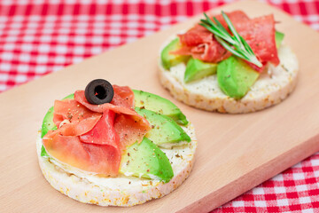 Rice Cake Sandwich with Avocado, Jamon, Olives and Rosemary on Wooden Cutting Board. Easy Breakfast. Quick and Healthy Sandwiches. Crispbread with Tasty Filling. Healthy Dietary Snack