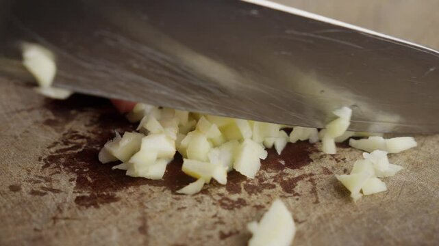 Person chopping garlic on a cutting board, close-up showing hands and minced garlic pieces, preparing ingredients