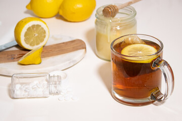 Hot tea with fresh lemon and honey, a bottle with white pills on white table