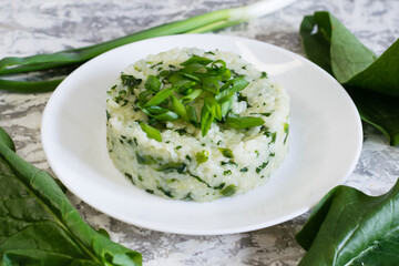 Vegan, vegetarian delicious dish. Rice with spinach and onions on a white plate close-up, fresh spinach leaves on the table. Concept of healthy eating