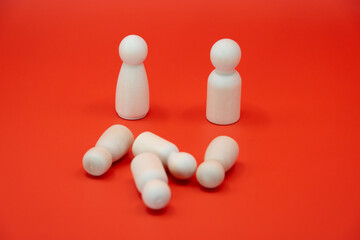 This image presents a minimalist scene featuring two upright wooden figurines standing over four other figurines that are laying down on a bright red background. 