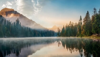 Fototapeta premium Sunrise is reflecting on a lake surrounded by a forest covered by fog