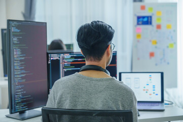 Asian software developers working on multiple screens displaying code and application diagrams in a...