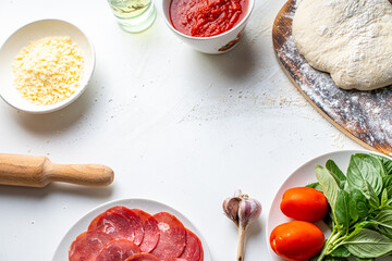 Ingredients for making Italian pizza: dough, tomato sauce, parmesan, tomatoes, basil, garlic, sausage on a white table. Real pizza recipe. Copyspace