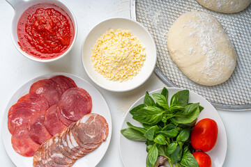 Ingredients for making Italian pizza: dough, tomato sauce, parmesan, tomatoes, basil, garlic, sausage on a white table. Real pizza recipe