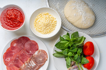 Ingredients for making Italian pizza: dough, tomato sauce, parmesan, tomatoes, basil, garlic, sausage on a white table. Real pizza recipe