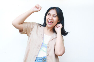 happy asian woman celebrate victory with raised fist wearing casual brown clothes isolated on white background