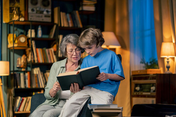 a warm light of living room with library big blue armchair elderly woman sitting with grandson...