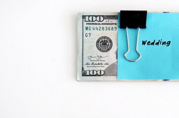 Cash money in dollars clipped with a blue note written WEDDING on white background with copy space  - concept of saving or planning budget for wedding day