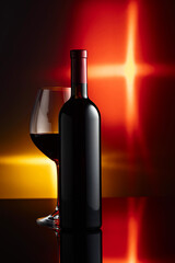 Glass and bottle of red wine on a black reflective background.