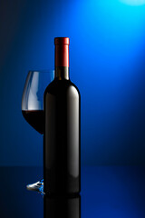 Glass and bottle of red wine on a blue background.