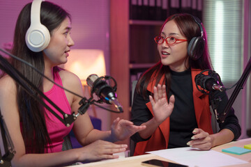 Two beautiful women chat while co-hosting an audio broadcast in a home studio. Recording internet podcasts for social media channels Ideas for creating online work.
