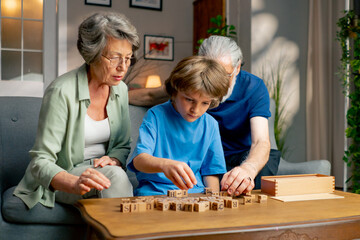 a bright living room with sofa grandpa and grandma sitting with grandson on table collecting words from cubes hand motor skills mind training