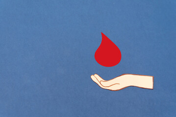 paper cutout Hand holding a red blood drop on a dark blue background, blood donation concept