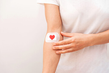 Close up of Person Touching a Bandage with Red Heart on Arm After Medical Procedure on grey...