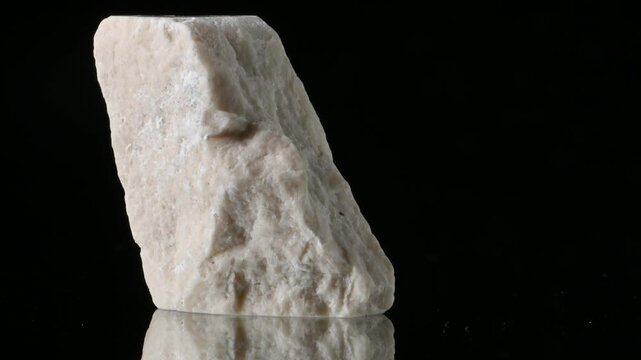 White aragonite (calcium carbonate) sample rotating against a black background