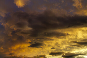 Obraz premium With a typhoon approaching, the sky features a dramatic cloudscape with dark, brooding clouds illuminated by a warm, golden light. The contrasting shadows and highlights create a moody atmosphere.