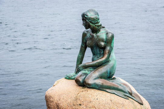 Copenhagen, Denmark - July 16, 2024: The Little Mermaid is a bronze statue by Edvard Eriksen depicting the character in the 1837 fairy tale by H.C. Andersen, displayed since 1913 on a rock by the sea.