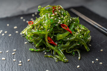 Japanese seaweed salad with sesame seeds and chili peppers on a black mica board with chopsticks.