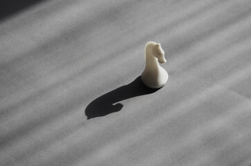 A white chess knight in bright sunlight casting a black shadow on a gray background, unconventional thinking, surprise and flexibility, freedom of thought, risk and adventurousness. © Александр Ланевский