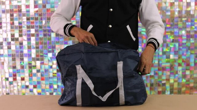 Person places sewing machine inside large blue travel bag against colorful background