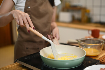 Cropped shot young woman cooking scrambled eggs in a frying pan on an electric stovetop