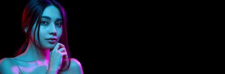 Portrait of beautiful young Korean woman with well-kept spotless skin posing against black background in neon light. Concept of natural beauty, skincare, cosmetics and cosmetology