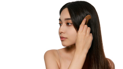 Fototapeta premium Young Korean girl taking care after her hair, using wooden hair brush, combing hair isolated on white background. Concept of natural beauty, skincare, cosmetics and cosmetology