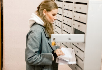 A young blonde woman checks the mailbox in the entrance of an apartment building.