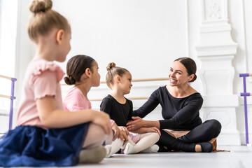 Female professional teacher instructing group of young ballerinas o classical dance indoors