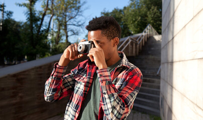 Young african man taking picture with camera, creative black american guy photographer in the city