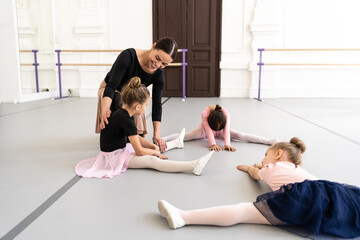 Woman trainer of ballet school helps young ballerinas perform different choreographic exercises