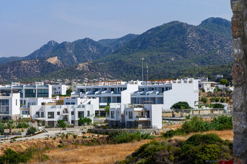 Obraz premium Modern white buildings contrast with rugged mountains in a quiet hillside community during a sunny afternoon