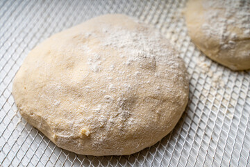 Pizza dough on a pizza baking wheel on a white table.