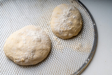 Pizza dough on a pizza baking wheel on a white table.