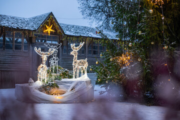 Luminous reindeer figures standing outside wooden house covered snow winter holiday season,...